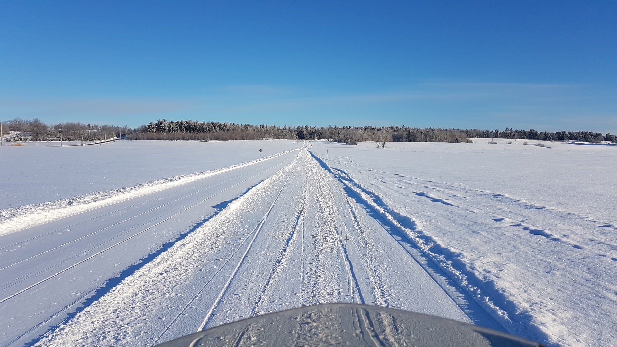 Snowmobile trail through a snowy field under a blue sky
